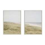 Two framed canvas prints side by side showing a calm coastal landscape with sand dunes and grassy hills under a pale sky, the right print includes a glimpse of the ocean.