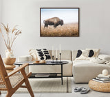 Framed canvas above beige sectional sofa showing a solitary American bison in tall prairie grass under a clear sky, in a neutral-toned modern living room.