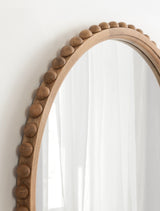 Round wall mirror with a natural wood frame featuring evenly spaced spherical wooden beads around the perimeter, reflecting sheer white curtains.