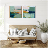 Two framed abstract paintings with teal, navy, peach, and white blocks hung above light wood bench with white cushion and gray check pillows in a white paneled room.