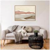 Neutral-toned living room with a beige sofa featuring a hound dog, round beige pillow, gray throw, black rattan side table with a small green plant, and an abstract landscape artwork in browns above.