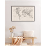 Vintage-style black and white world map framed on wall above wooden bench with white cushions, beige throw, and vase with dried flowers.
