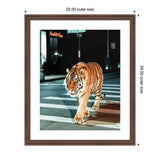 Photo of a tiger walking across a city street crosswalk at night, framed with a white mat and dark brown wood frame, with illuminated signs in the background.