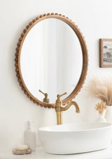 Round wall mirror with a natural wood frame featuring evenly spaced wooden beads along its edge, reflecting a brass faucet over a white oval sink in a neutral bathroom setting.