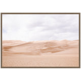 Softly lit pale desert dunes under a cloudy sky, framed in a simple muted wooden frame, showcasing smooth sand textures and gentle slopes.