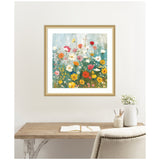 Square framed painting of a wildflower garden with yellow, red, white, and pink flowers against a soft blue and green background, hanging above a wooden desk with a book and white vase.