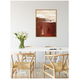 Abstract framed canvas featuring warm earth tones with layered brushstrokes in brown and beige, hanging on a white wall above a white table with four natural wood chairs.