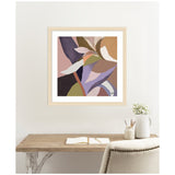 Abstract botanical artwork with overlapping shapes in muted tones of purple, pink, green, and tan, framed in light wood and hanging above a minimalist desk setup.