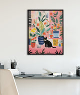 Colorful illustration of various potted houseplants with green leaves and yellow, orange, pink flowers surrounding a black cat with yellow eyes on a pink background, framed on a white wall above a desk.