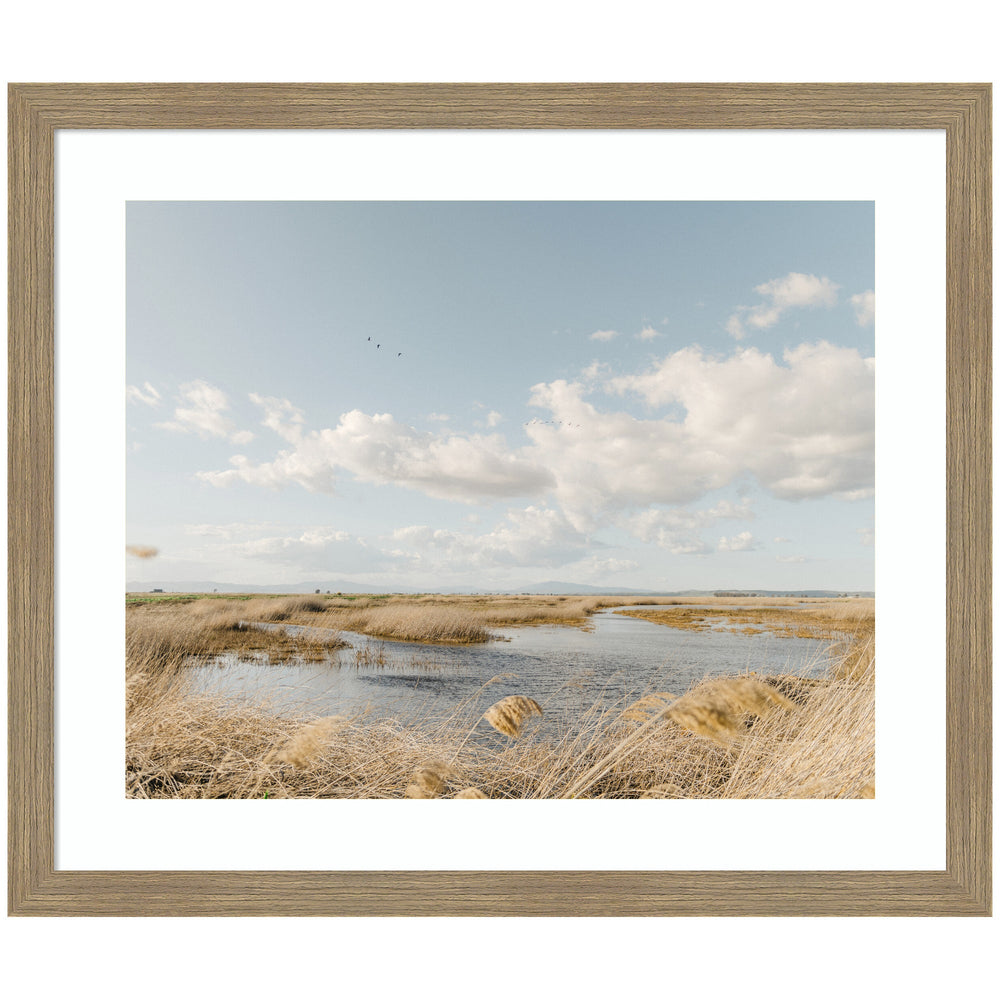 Framed art print titled Marshland by Crystal Lynn Collins showing a marsh landscape with waterway and golden reeds under a vast sky with scattered clouds