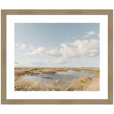 Framed art print titled Marshland by Crystal Lynn Collins showing a marsh landscape with waterway and golden reeds under a vast sky with scattered clouds