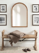 Arched wood-framed wall mirror above a wooden bench with a textured taupe throw blanket, surrounded by four black-and-white framed photographs on a cream wall.