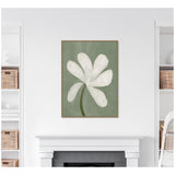 Framed canvas print of a large white flower with six curved petals and a green stem on a muted green background, centered above a white mantle and fireplace.