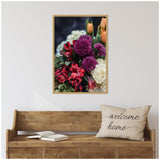 Framed canvas with close-up of vibrant purple, red, peach, and white flowers hanging above a rustic wooden bench with a beige 'welcome home' pillow and open book.