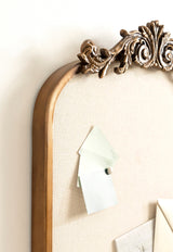 Arched pinboard with ornate carved wood top detail and light fabric surface holding pinned color swatches and paper notes.