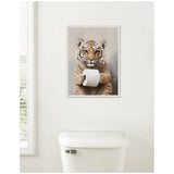Framed canvas artwork of a tiger cub holding a white toilet paper roll, hung on a white bathroom wall above a white toilet tank.