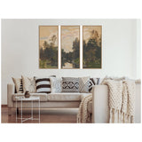 Three-panel framed canvas art depicting a river flanked by dark green trees under a cloudy, soft yellow sky, hung above a beige couch with patterned pillows and a chunky knit throw.
