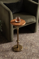 Small round wooden side table with brass adjustable stem and round base, next to an olive-green upholstered armchair with a dark pillow