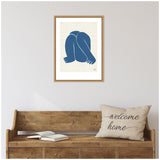 Framed minimalist artwork depicting a crouched figure in solid blue, hanging above a wooden bench with a 'welcome home' pillow and open book.