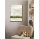 Vertical framed canvas painting showing a soft green forest line under a cloudy sky with a flock of flying birds in muted earth tones, hanging above a beige textured chair with a gold gift box.