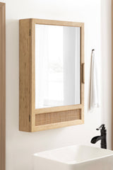 Wall-mounted rectangular wooden cabinet with a large mirror front and a woven rattan panel at the bottom, shown above a white sink and black faucet.