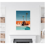 Photograph of a bison resting by a turquoise pool with an orange wall and palm trees under a clear blue sky.