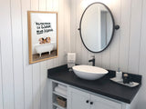 Bathroom with white vertical panel walls, black countertop holding an oval white vessel sink, round wall mirror, and framed print of three piglets in a white clawfoot bathtub with text.