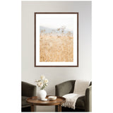 Wall art featuring delicate beige wild fennel plants with soft-focus hills in background, framed in dark wood above a cozy seating area with green chairs and a round wooden table.