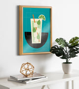 Framed abstract art print featuring a stylized mojito with lime wedge and mint leaves on a teal background, hanging above a white shelf with a plant and geometric decor.