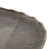 Close-up of a round tray with a textured, speckled surface and irregularly scalloped rim in muted gray tones, showing subtle variations in finish.