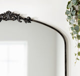 Upper corner of a traditional arch mirror with ornate black metal frame detail and trailing green vine with heart-shaped leaves on the right side.