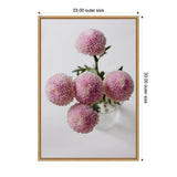 Top-down view of five pastel pink dahlia blooms with green stems arranged in a clear glass vase against a white background, framed in natural wood.