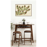 Framed canvas wall art featuring a botanical branch with brown pine cones and green leaves, hung above a wooden high table with two matching stools and minimalist decor.