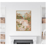 Framed canvas artwork depicting a sandy beach path with grass and wildflowers under a soft sunrise sky in muted earthy tones, hung above a white mantel.