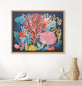 Framed print of colorful coral and seaweed in shades of pink, red, yellow, and blue on a dark background, hanging above a beige shelf with seashell and starfish decor.