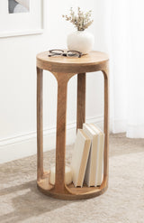 Tall round wooden drink table with four vertical pillars creating a lower shelf holding three books, topped with a small white vase and glasses beside it.