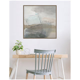 Abstract framed canvas wall art featuring soft gray, beige, and muted blue tones with sweeping brushstrokes, hanging above a light wood desk with a pale blue chair.