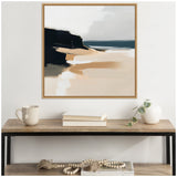Abstract coastal landscape painting with sandy beige foreground, dark cliffs on left, and blue-gray water horizon, framed and hanging above a shelf with books and plants.