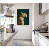 Framed canvas print of a gilded cheetah profile on emerald green background hanging on kitchen wall with white cabinets and gray stone countertops.