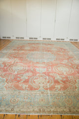 Vintage Mahal carpet in faded coral and light blue with a central medallion and intricate floral patterns, laid on wooden floor against white paneled wall.