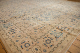 Faded vintage Mahal carpet in beige and muted blue tones with floral and geometric motifs, shown angled on a wooden floor.