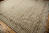 Large vintage Sivas carpet with distressed beige and brown geometric and floral patterns, bordered with multiple intricate bands, laid on wooden flooring.