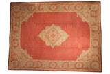 Rectangular vintage Oushak carpet in faded coral red with cream floral medallion center and intricate border patterns.