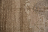 Close-up of a vintage distressed Oushak carpet with beige and brown tones, featuring a faded geometric and floral pattern with a textured weave.
