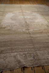 Vintage distressed Oushak carpet in muted beige and cream tones with a faded central medallion pattern laid on wooden floorboards.