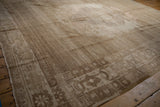 Distressed vintage Oushak carpet in muted beige tones with intricate faded floral and geometric patterns, laid on a wooden floor with warm lighting.