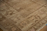 Close-up of a vintage distressed Oushak carpet with a faded brown and beige floral pattern and subtle pink accents along the edge on wooden flooring.