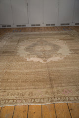 Large vintage distressed Oushak carpet with faded beige and light brown tones featuring a central medallion pattern on a wooden floor.