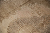 Close-up detail of a vintage distressed Oushak carpet showcasing faded geometric and floral patterns in muted beige and brown tones.