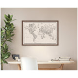 Vintage black and white linen world map with detailed countries and borders inside a dark wooden frame, hanging on a beige wall above a white desk with books and a green plant.